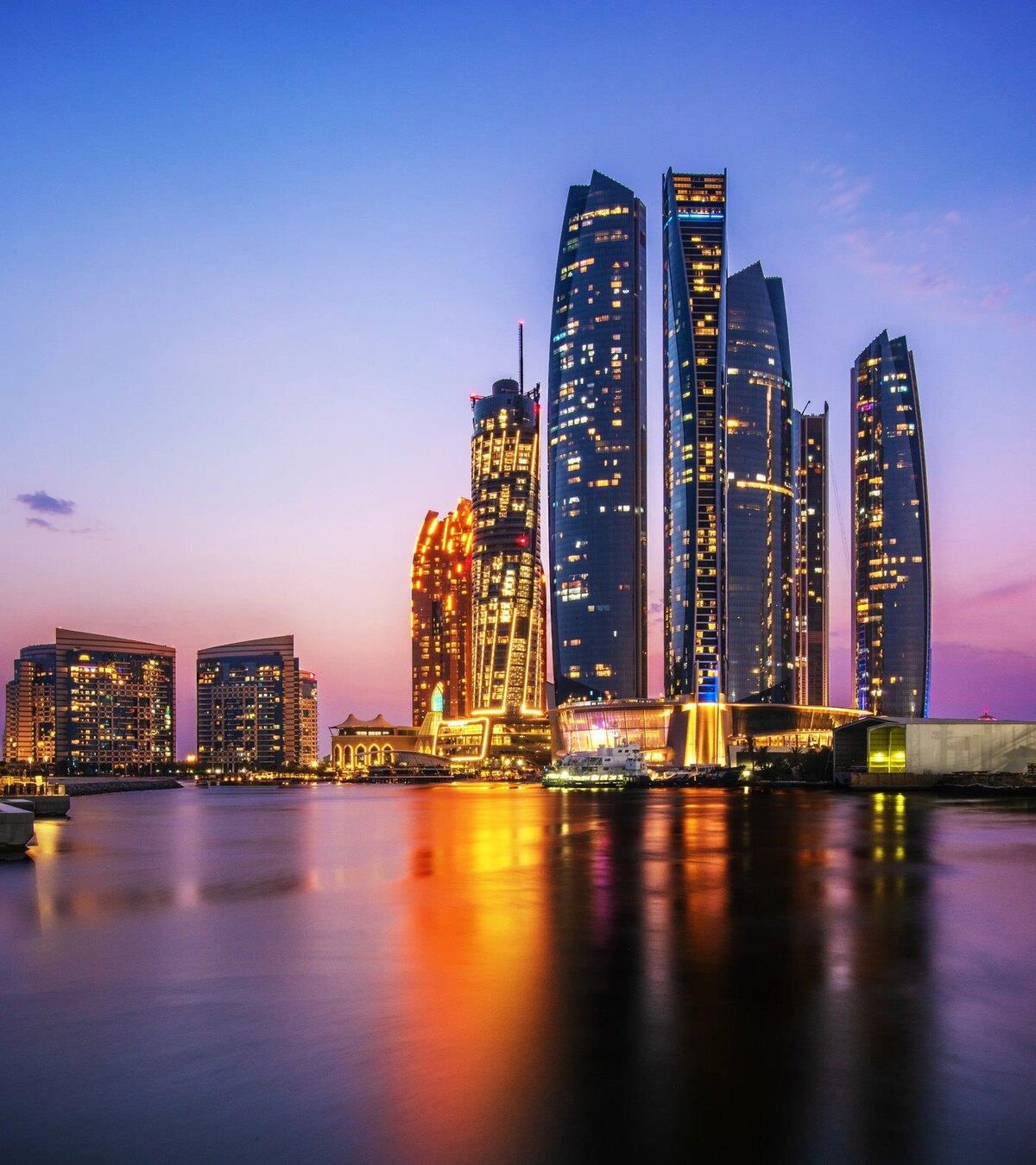 Abu Dhabi's Etihad Towers at dusk, reflected in the water; photograph of the city, not the project.